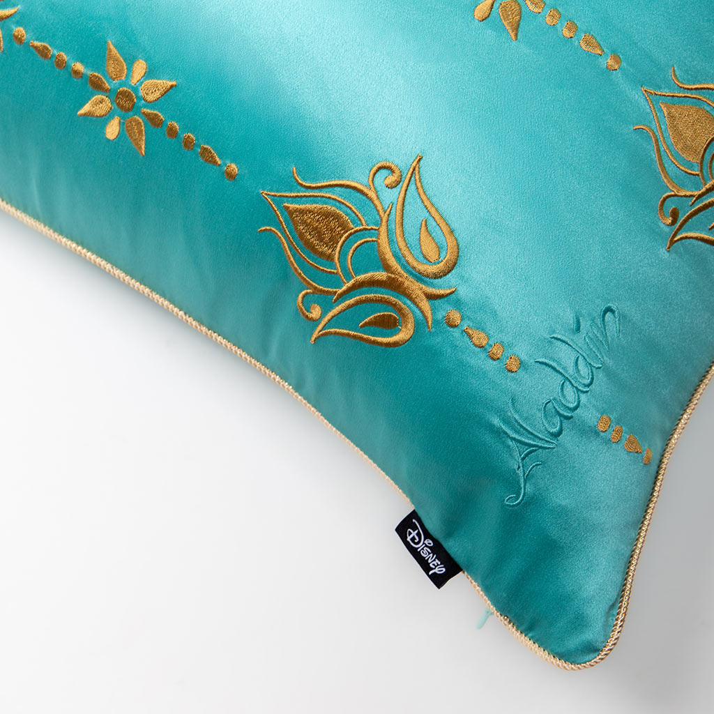 The Jasmine Cushion Cover by drowsysleepco features a turquoise blue design with gold embroidery, "Aladdin" detail, gold trim, black Disney tag, and is made from luxurious mulberry silk.