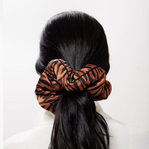 A person with long dark hair in a low ponytail, secured with the Rajah Padded Scrunchie by drowsysleepco in orange and black zebra stripes, wears a white top. Photographed from the back, this accessory offers effortless style and hair protection.