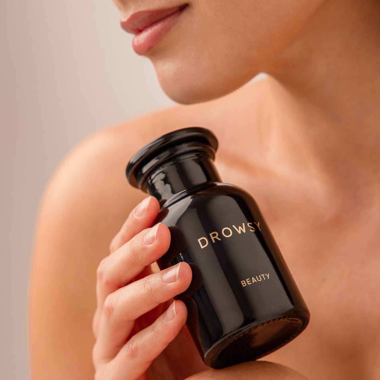 A person holds a black Apothecary Glass Storage Jar by drowsysleepco near their chin, with soft lighting highlighting their smooth skin and relaxed pose.
