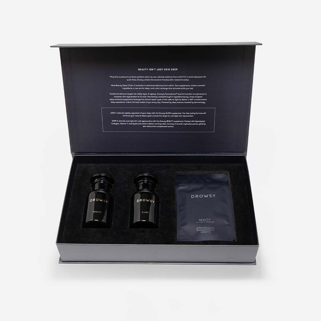 An open black box from drowsysleepco displays two black jars and a packet labeled Supplements - Beauty Sleep Clinic, arranged in foam. The inside lid features product information printed in white text.