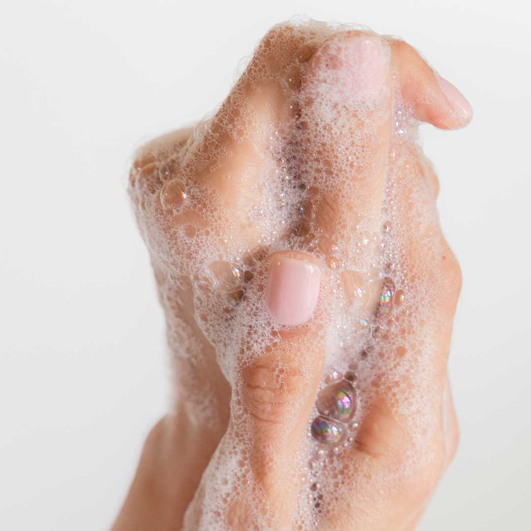 A close-up of a hand with neatly manicured nails covered in foamy drowsysleepco Beauty Sleep Body Cleanser, set against a plain white background.