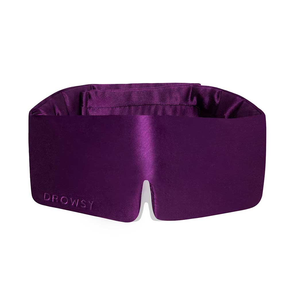 The Purple Martini silk sleep mask by drowsysleepco features a deep purple shade, wide blackout design, and nose cutout for comfort—perfect for uninterrupted beauty sleep. DROWSY is embossed on the lower left corner.
