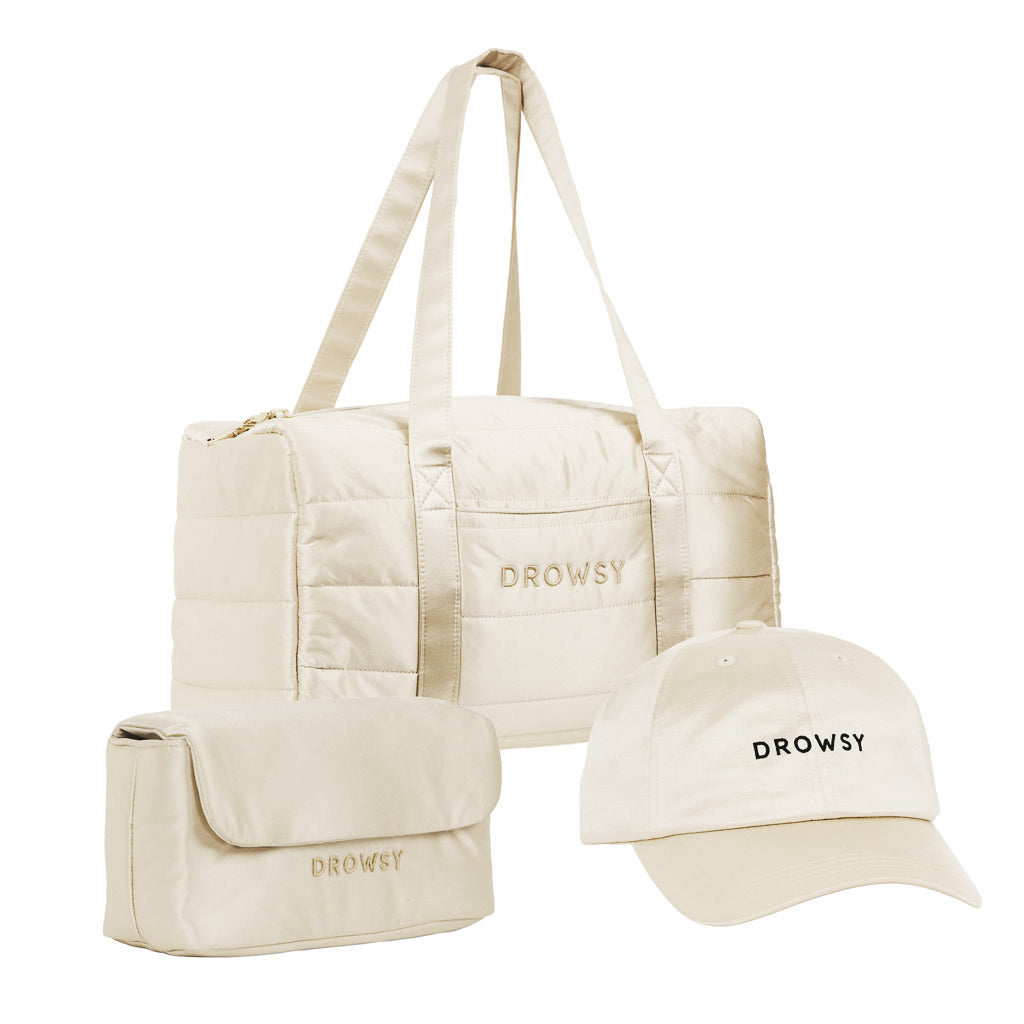 The Drowsy Weekend Collection - Dusty Gold by Drowsy features a beige quilted duffel, matching toiletry bag, and beige cap—all embroidered with “DROWSY” in black—set against a white background.