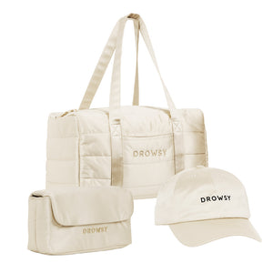 The Drowsy Weekend Collection - Dusty Gold by Drowsy features a beige quilted duffel, matching toiletry bag, and beige cap—all embroidered with “DROWSY” in black—set against a white background.