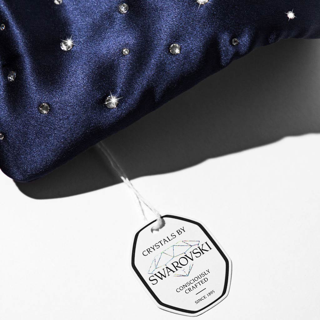 The drowsysleepco Silk Sleep Mask Crystals by Swarovski® is a navy blue satin eye mask adorned with shimmering crystals and a white “Crystals by Swarovski, Consciously Crafted, Since 1895” tag on a white background.