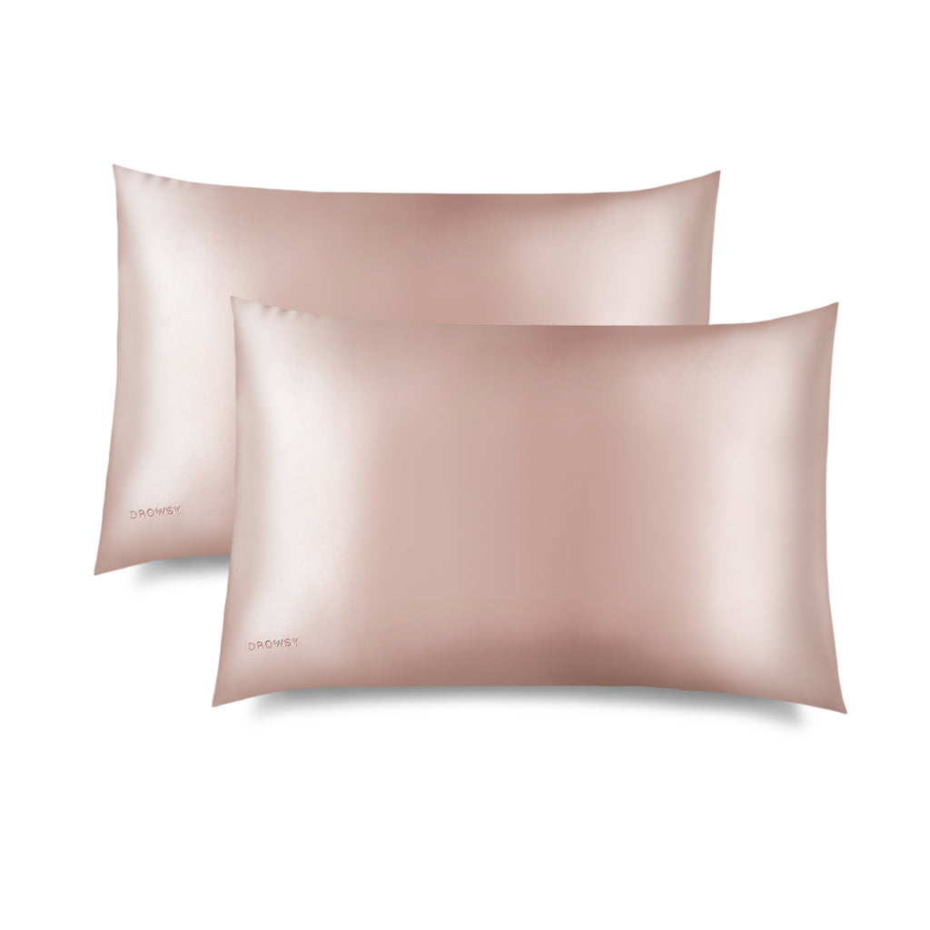 Two Sunset Pink Silk Pillowcases by drowsysleepco sit overlapping on a white background. Their smooth, shiny silk helps protect hair and support skincare, with a subtle drowsysleepco logo in the lower left corner.