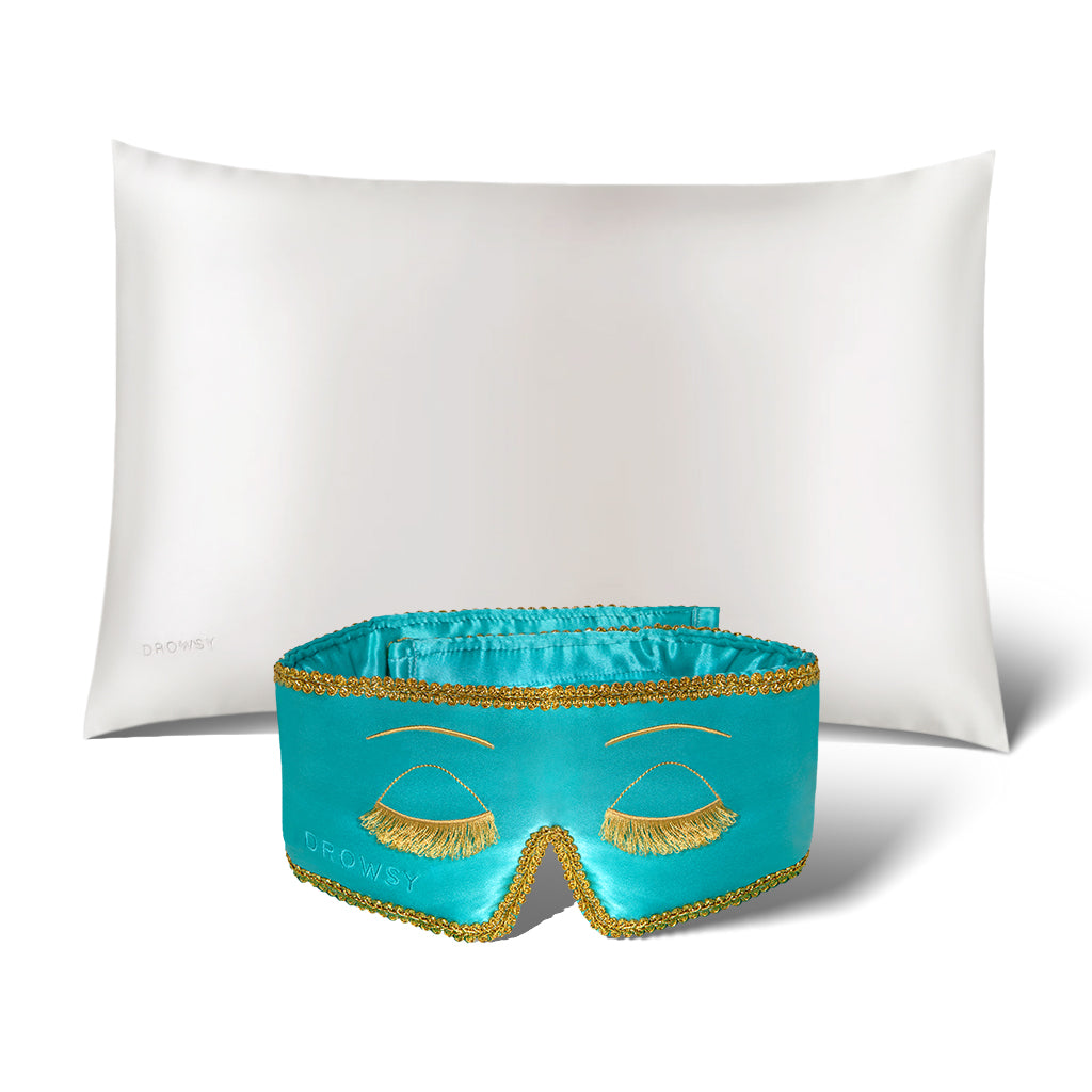 The Perfect Skin Bundle Breakfast at Drowsy by drowsysleepco showcases a white silk pillowcase and a turquoise sleep mask with gold embroidered eyelashes, set against a white background—ideal for elevating your beauty sleep.