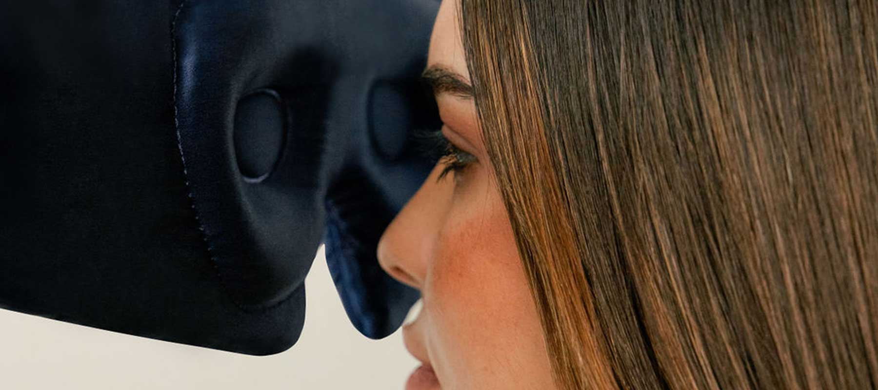 A woman with straight brown hair is pressing her face against a dark blue padded object, possibly a massage or relaxation device, with her eyes closed.