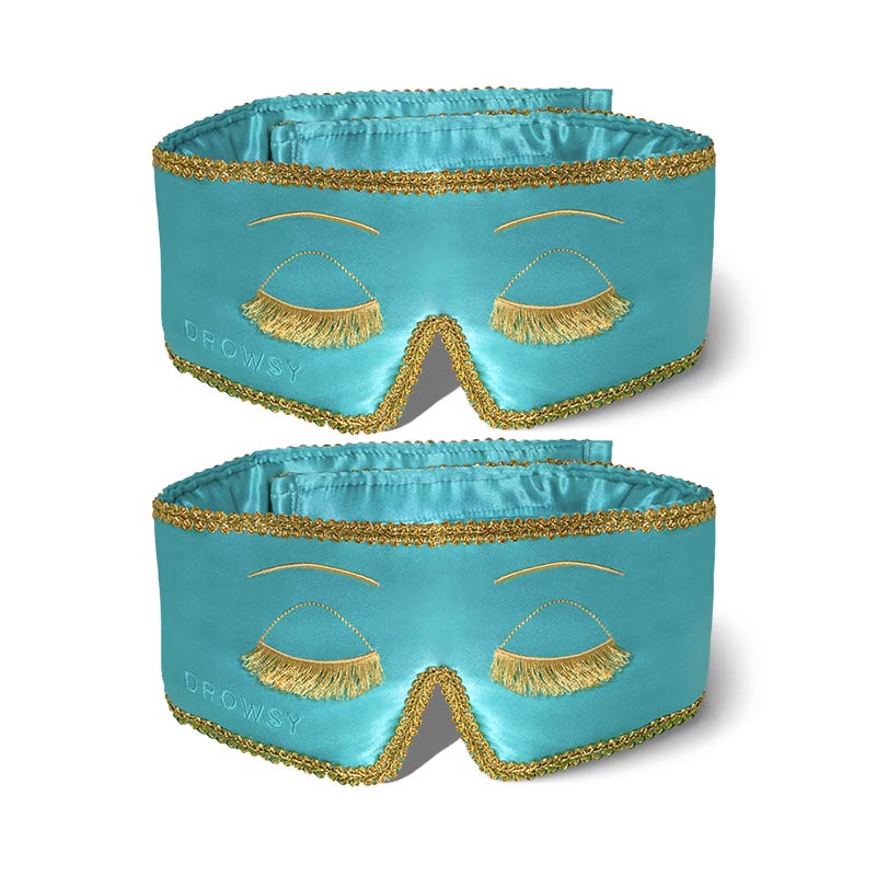 The drowsysleepco 2-Pack Sleep Masks | Breakfast at Drowsy features turquoise masks with gold fringe and trim, resembling closed eyelashes, and “Drowsy” embroidered on the lower left corner, displayed flat on a white background.