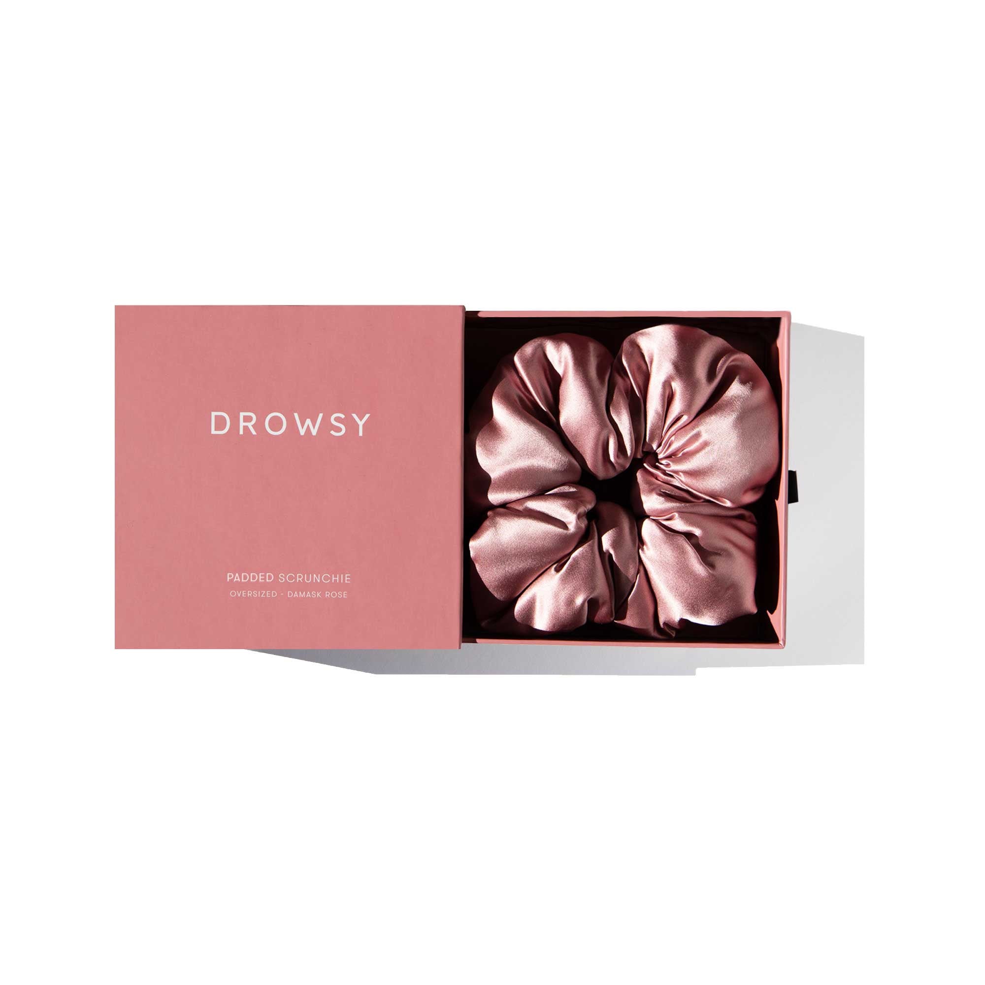 The Damask Rose - Padded Scrunchie by drowsysleepco, an oversized pink silk accessory, is displayed inside its matching pink DROWSY box on a white background.
