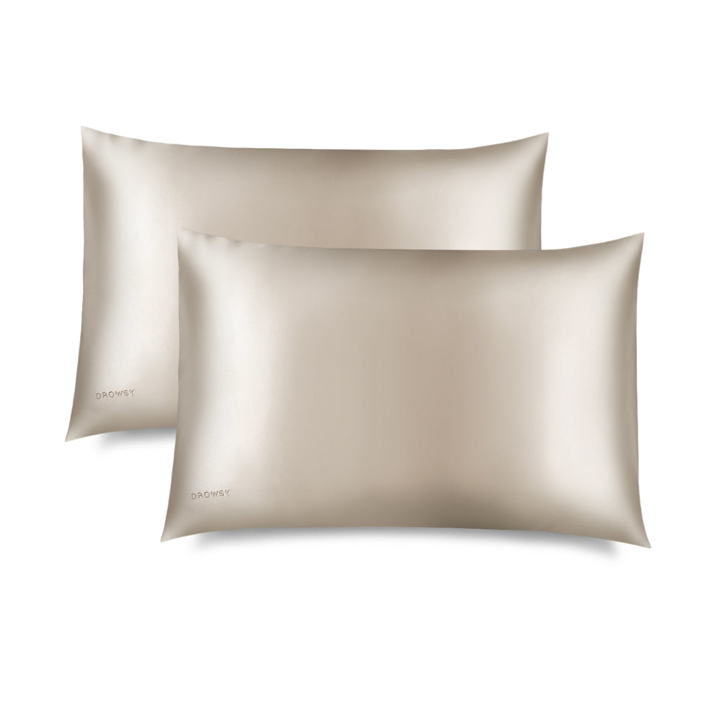 Two Dusty Gold Silk Pillowcases with a subtle sheen is displayed on a white background. DROWSY appears in small letters at the bottom left—a hair-protecting, skincare-essential silk pillowcase.