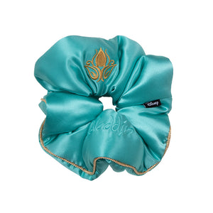 The Jasmine Padded Scrunchie by drowsysleepco is a teal satin hair accessory with gold lotus and "Aladdin" embroidery, gold-trimmed edges for volume, and a small black Disney tag on the side.