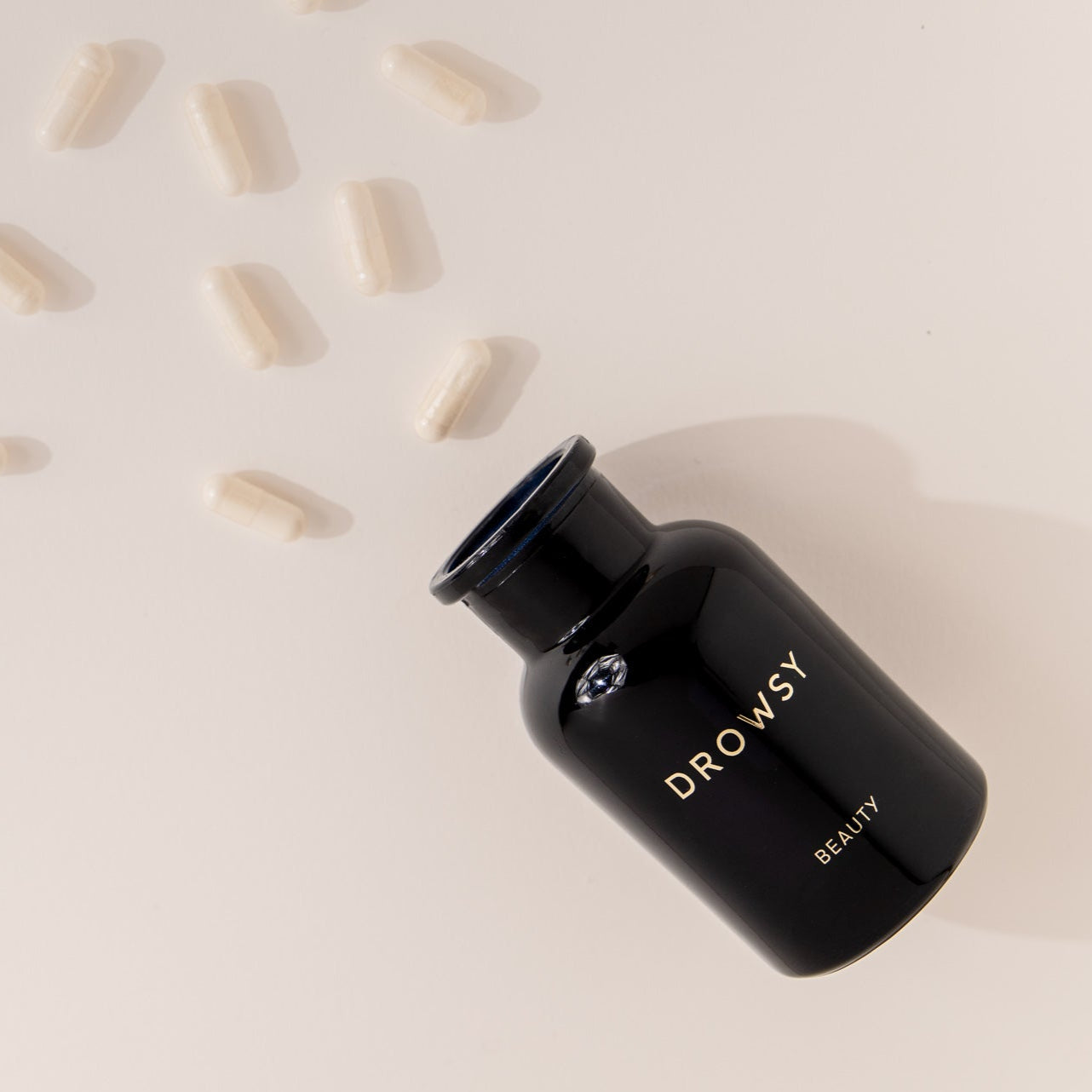 A black Apothecary Glass Storage Jar by drowsysleepco lies on its side with the lid off, spilling several white capsules onto a light surface.