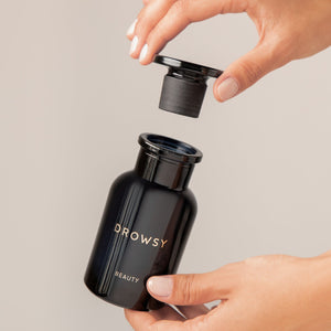A person lifts the lid of a sleek, black Apothecary Glass Storage Jar from drowsysleepco with one hand while holding the jar with the other against a neutral background.