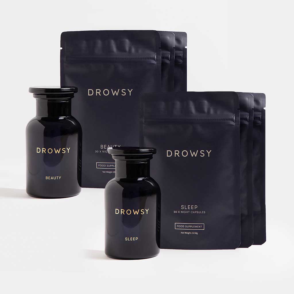 Two dark glass jars labeled Supplements - Beauty Sleep Clinic by drowsysleepco, one for Beauty and one for Sleep, sit before matching black pouches featuring the brands logo, displaying this restorative sleep and skin supplement set on a white background.