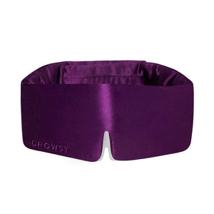 The Purple Martini silk sleep mask by drowsysleepco features a deep purple shade, wide blackout design, and nose cutout for comfort—perfect for uninterrupted beauty sleep. DROWSY is embossed on the lower left corner.