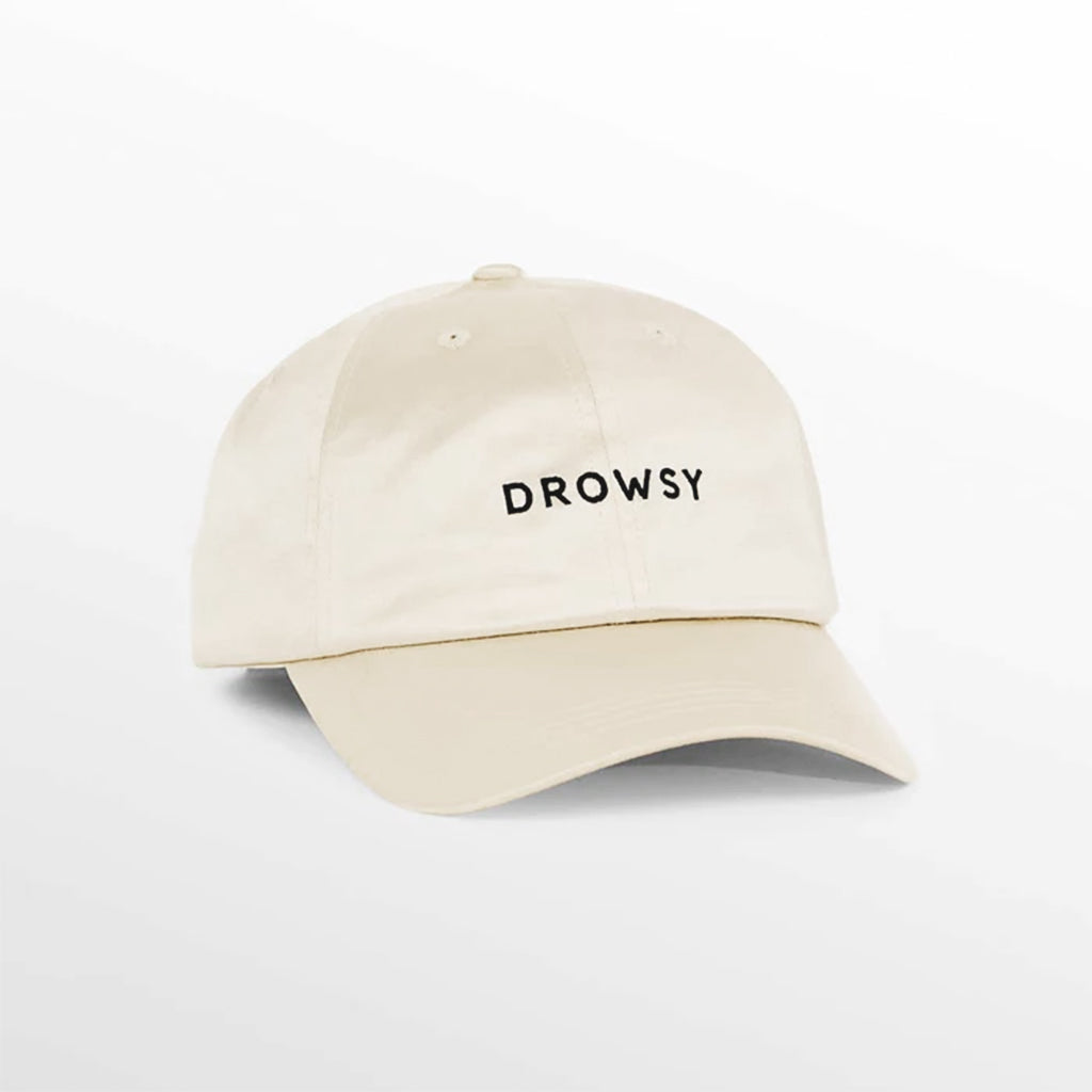 The Drowsy Silk Cap in Dusty Gold by Drowsy features black "DROWSY" embroidery on the front, offering sun shielding and light hair protection. Displayed against a plain white background.