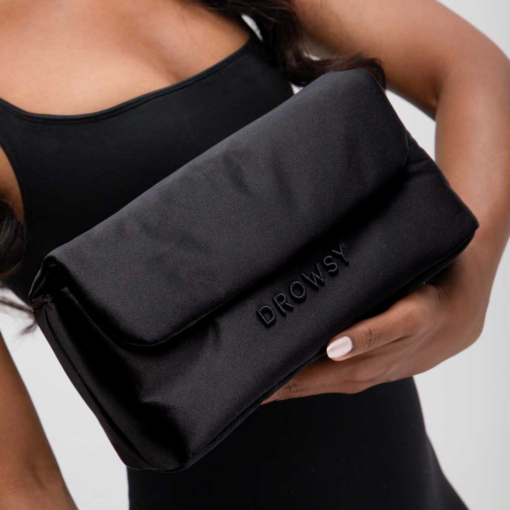 A person in a black sleeveless top holds the drowsysleepco Perfect Escape Bundle - Black Jade, featuring a large pouch ideal for storing your luxurious silk sleep mask for ultimate beauty rest.