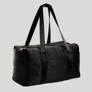 The Drowsy Silk Weekender - Black Jade by Drowsy features black quilted silk, two long shoulder straps, a gold zipper, and DROWSY embroidery on the front. This spacious bag is shown against a plain gray background.