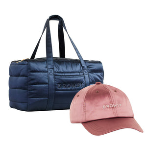 The Drowsy Roadtrip Bundle, featuring a midnight blue quilted duffel bag and a damask rose pink cap, both embroidered with “DROWSY,” is displayed on a white background.