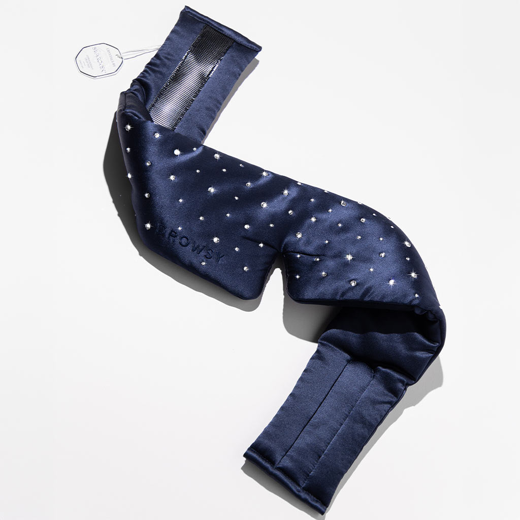 The Silk Sleep Mask Crystals by Swarovski® from drowsysleepco is a navy blue satin blackout mask with small white dots, adjustable straps, and a tag, shown on a white background.
