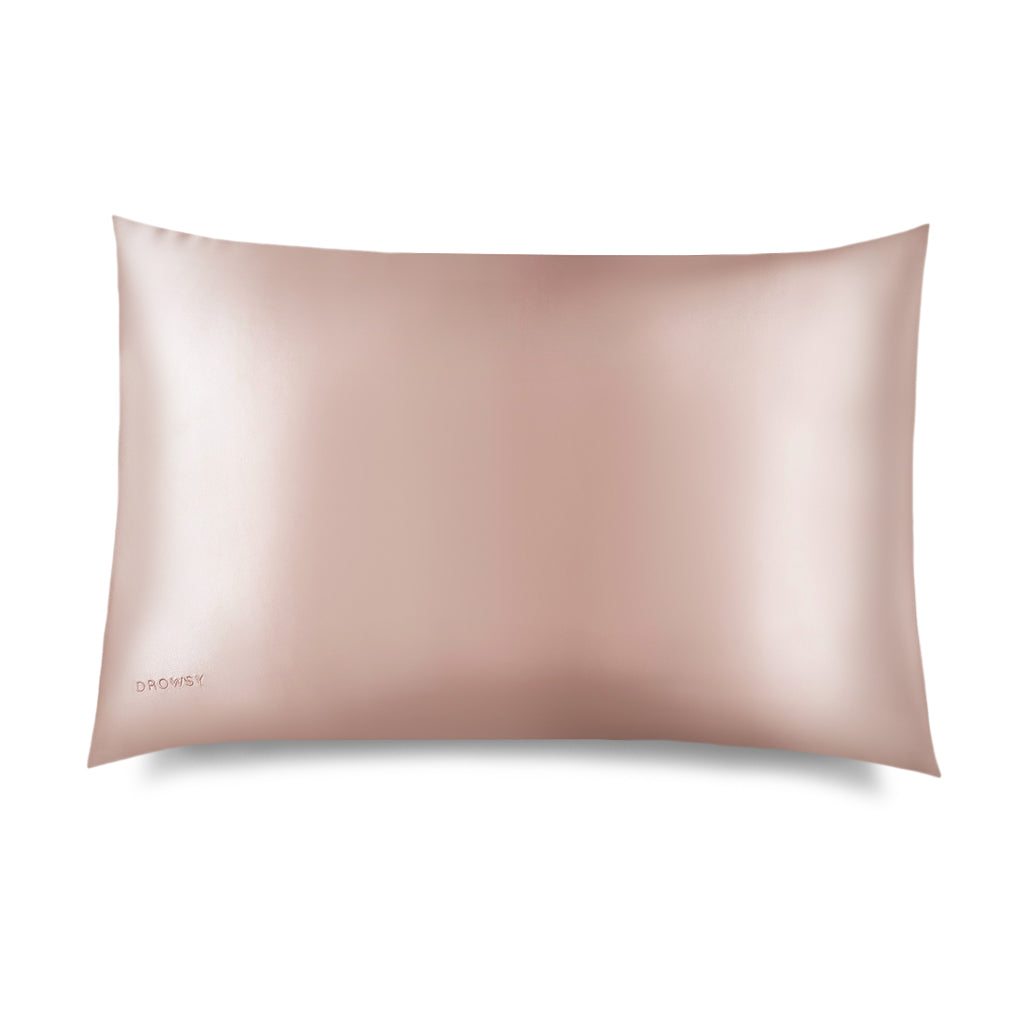 The Sunset Pink Silk Pillowcase by drowsysleepco is a smooth, rectangular, light pink silk case with a subtle sheen, designed for hair and skin benefits, featuring a small DROWSY logo in the bottom left corner on a white background.
