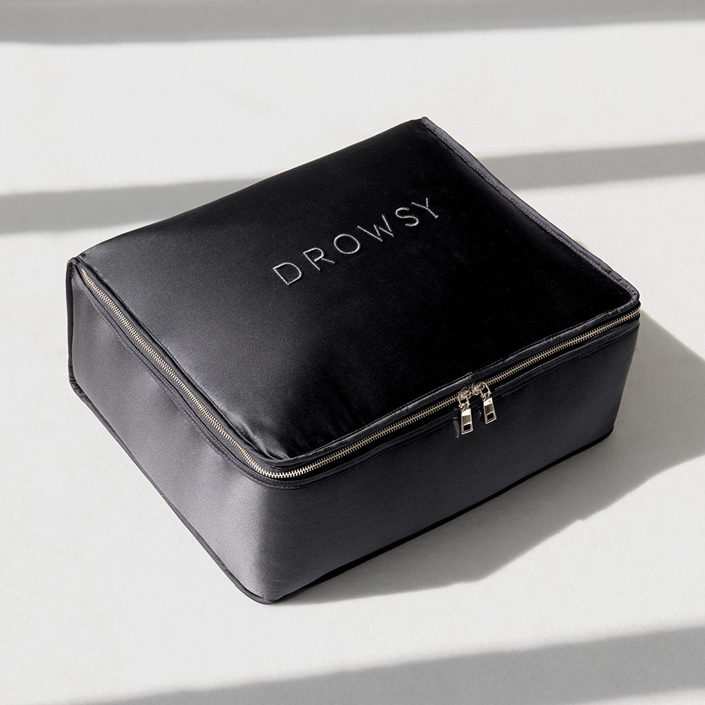 A black zippered rectangular pouch with "DROWSY" in white on top, placed on a light surface with shadows—ideal for storing the drowsysleepco Moonlight Shadow Silk Weighted Blanket.