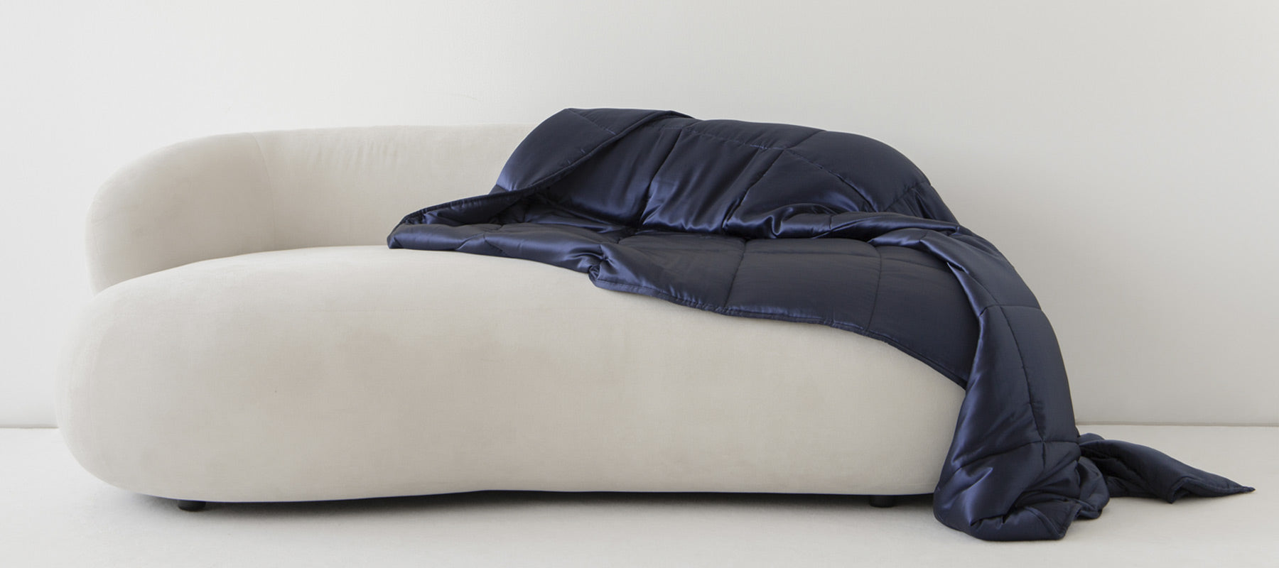 A navy blue blanket is draped over a modern, white, curved sofa against a plain white wall.