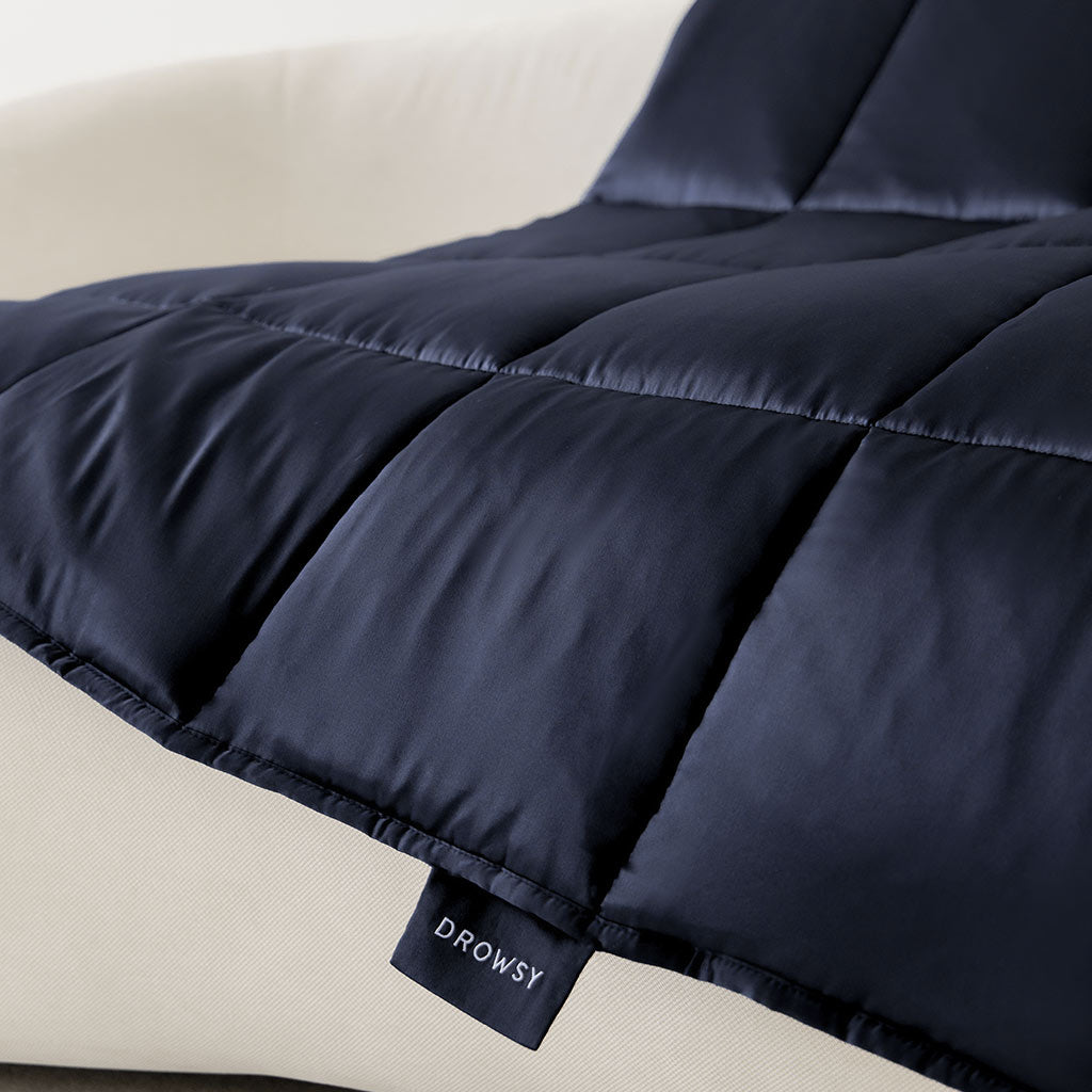 A close-up of the Midnight Blue Silk Weighted Blanket by drowsysleepco, draped on a light surface with a small “drowsysleepco” tag—an ideal choice for deep relaxation.