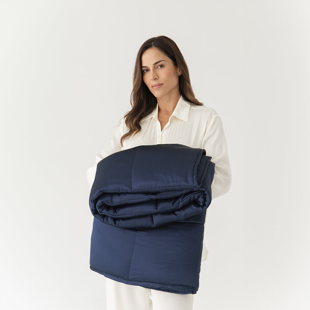 A woman in white holds the drowsysleepco Midnight Blue Silk Weighted Blanket, folded, against a plain white background, evoking deep relaxation.