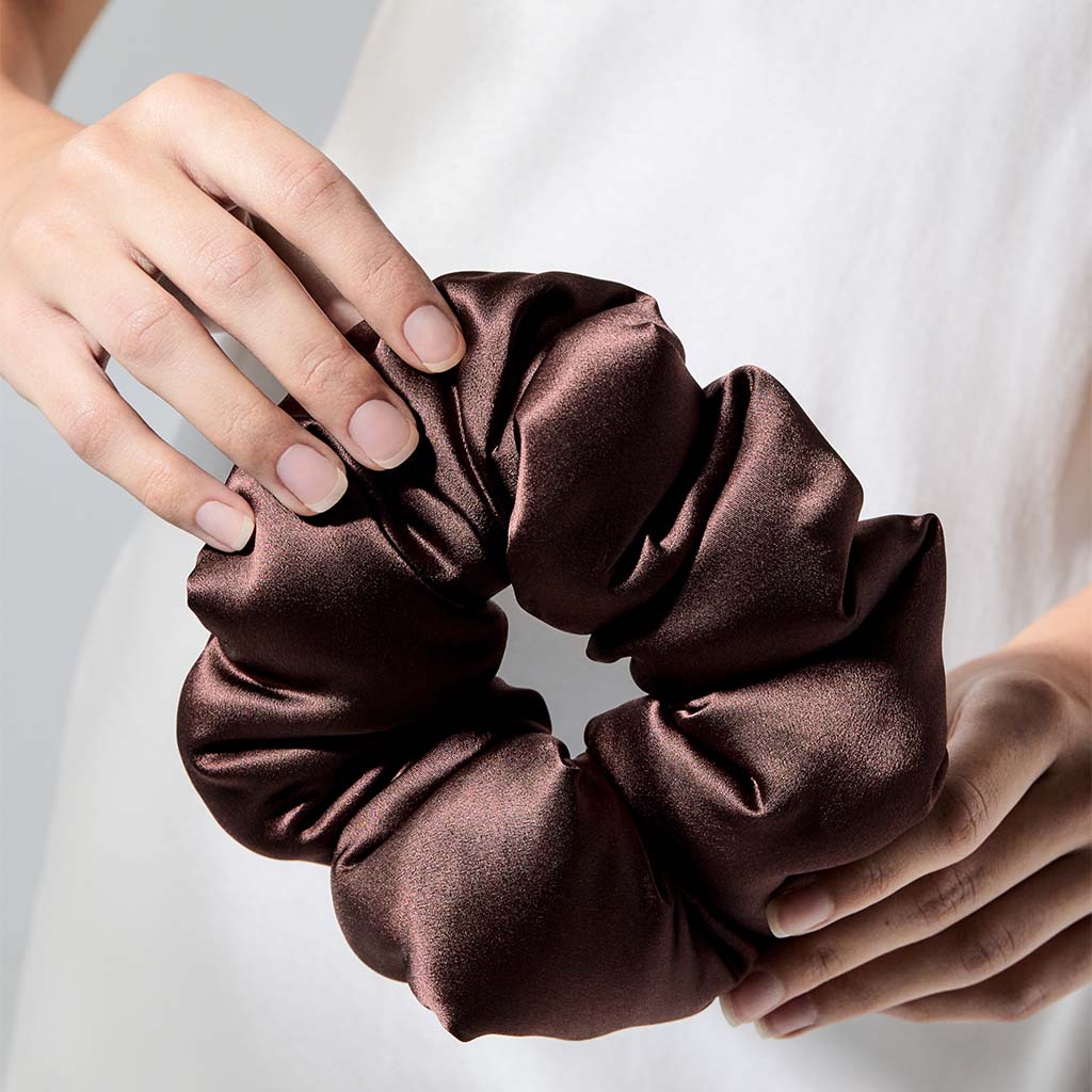 A person holds the drowsysleepco Cocoa Glow - Padded Scrunchie with both hands, displaying neatly manicured nails and wearing a white garment.