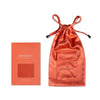 The drowsysleepco Summer Coral Silk Carry Pouch, made from orange mulberry silk with a drawstring and front pocket, sits beside its matching packaging. The box includes a fabric sample in the same vibrant shade as the pouch.