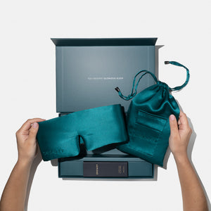 A person holds the drowsysleepco Green Sapphire Deep Sleep Collection silk mask and green pouch in front of an open gift box reading "YOU DESERVE GLORIOUS SLEEP," with a small product box inside, all set against a white background.