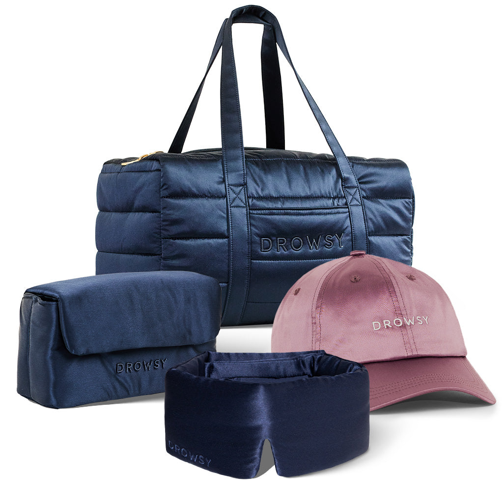 The Perfect Escape Bundle - Midnight Blue by drowsysleepco includes a navy duffel, matching toiletry bag, silk sleep mask, and dusty pink cap—all embroidered with DROWSY—displayed on white for a luxe travel set.