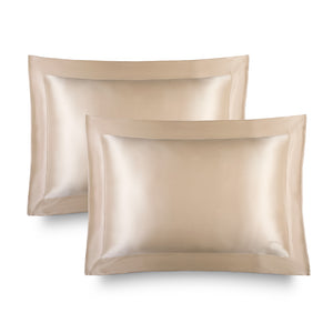 Two champagne gold, rectangular Hyalo Pillowcases by us.drowsysleepco with a smooth, lustrous finish are displayed side by side against a white background. Each pillowcase features a wide border and a subtle logo in the lower right corner, offering an elegant touch while supporting overnight hydration for your skin.