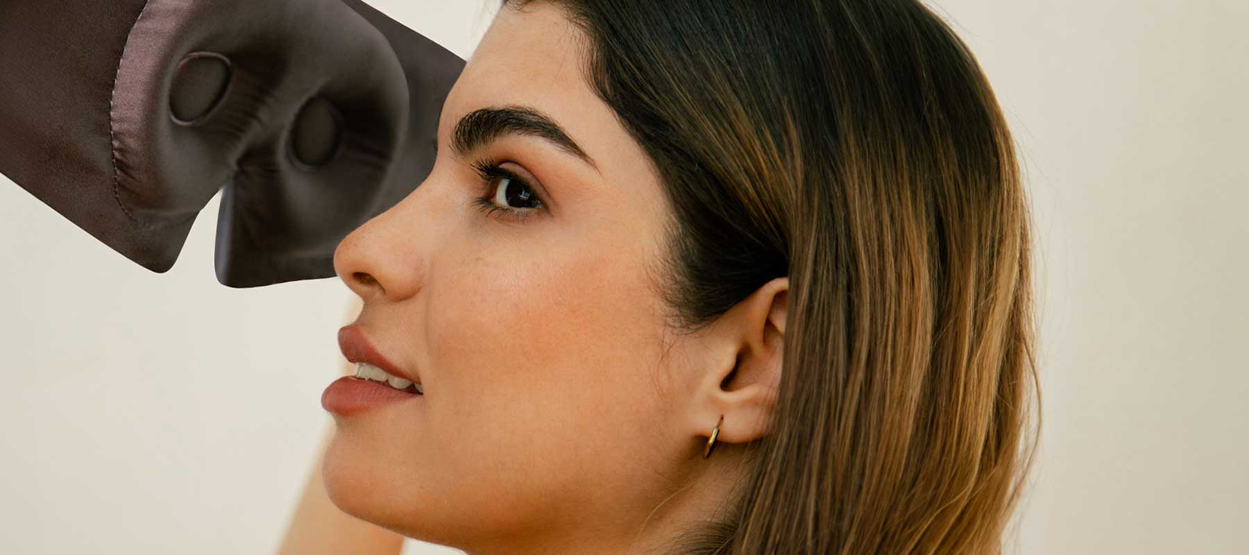 A woman with straight brown hair and gold hoop earrings looks forward and smiles slightly as a boxing glove approaches her face from the left side of the image.