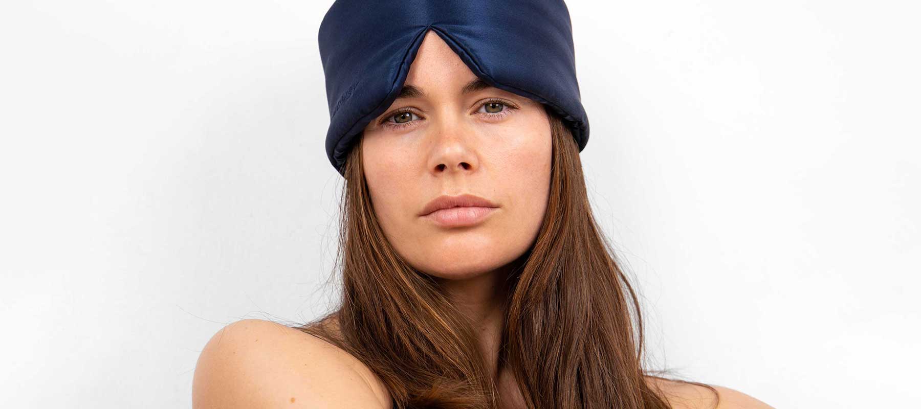 A woman with long brown hair wears a dark blue satin head wrap against a plain white background, looking directly at the camera with a neutral expression.